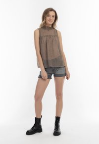 Bruine gebloemde mouwloze blouse met een hoge halslijn, gecombineerd met grijze denim shorts en zwarte veterschoenen tot de enkel. Gladde stofstructuur.