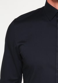 Donkerblauwe overhemd met knopen en een puntkraag, van gladde stof, met subtiele stiksels langs de knoopsluiting en schouders.