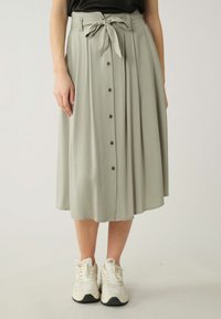 Jupe midi vert clair en tissu doux, dotée d'une ceinture à nouer, d'une fermeture à boutons à l'avant et d'un design plissé. Portée avec des baskets blanches.