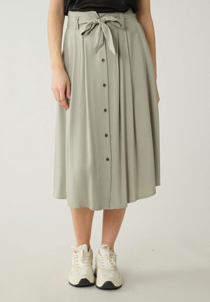 Jupe midi vert clair en tissu doux, dotée d'une ceinture à nouer, d'une fermeture à boutons à l'avant et d'un design plissé. Portée avec des baskets blanches.