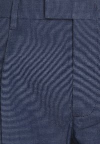 Tela de color azul marino con un patrón, que presenta una textura de cuadrícula, con un frente plano, bolsillos laterales y un corte ajustado.