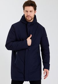 Veste bleu marine avec capuche, dotée d'une fermeture éclair sur le devant et de poches latérales. Fabriquée dans un matériau lisse et résistant avec une coupe décontractée.