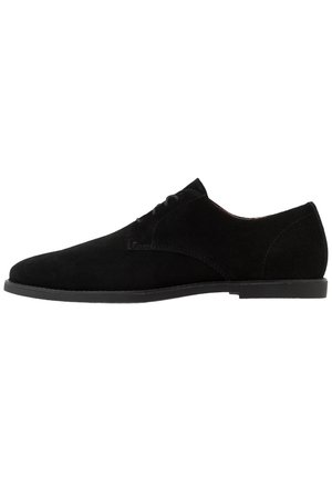Scarpa da uomo in camoscio nero con lacci, tacco basso e cuciture semplici su sfondo bianco, vista laterale.