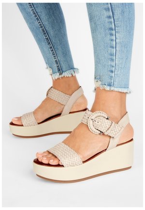 Beżowe plecione sandały na platformie z szerokim paskiem i okrągłą klamrą, wyposażone w piankową podeszwę i strukturalną górę, stylizowane z jasnoniebieskimi, postrzępionymi dżinsami.