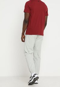 T-paita, jossa on lyhyet hihat viininpunaisena, yhdistettynä vaaleanharmaisiin kapeisiin housuihin ja musta-valkoisiin urheilukenkihin. Yksinkertainen, toiminnallinen muotoilu.