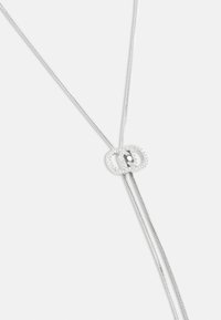 Collier en argent avec une chaîne élégante et flexible et un pendentif double ovale, orné de petites pierres claires autour du bord.