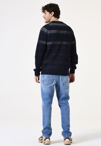 Jersey de punto a rayas azul marino con textura acanalada, cuello redondo y puños ajustados, combinado con jeans de color azul claro y zapatillas color beige.