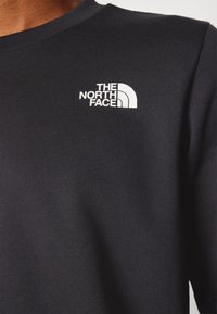Schwarzer Sweatshirt mit rundem Halsausschnitt, gerippten Bündchen und einem weißen Logo von "The North Face" auf der linken Brustseite. Weicher Stoff.