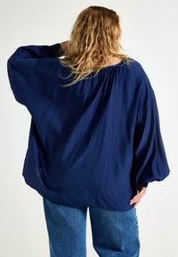 Marinblus med ett strukturerat mönster, vida ärmar och elastisk halsringning, tillsammans med ljusblå denimbyxor.