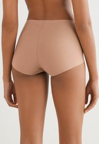 Béžové bezšvové šortky s vysokým pasem, hladkým povrchem, zaoblenými okraji a minimálním šitím, navržené pro pohodlí a těsné padnutí.