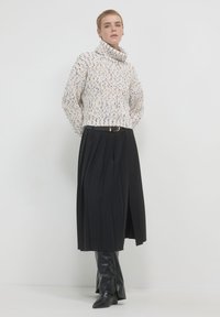Pull col roulé tricoté en crème avec des éclats multicolores, associé à une jupe plissée noire et des bottes noires jusqu'aux genoux.