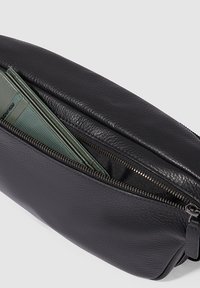 Schwarze Lederetui mit glatter Textur, ausgestattet mit einem Reißverschluss und teilweise sichtbarem grünen Geldbeutel im Inneren.