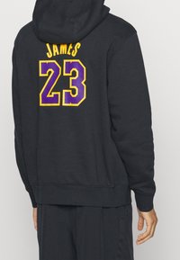 Hoodie noir avec capuche ; présente un texte imprimé en jaune et violet "JAMES" au-dessus du numéro "23" au dos ; poignets et ourlet côtelés.