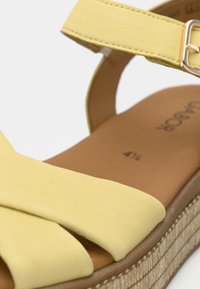 Κίτρινο σανδάλι με επάνω μέρος από υφασμένο δέρμα, διακοσμημένο με φαρδιά φιόγκο, λουράκι στον αστράγαλο και πλεκτή σόλα πλατφόρμας.