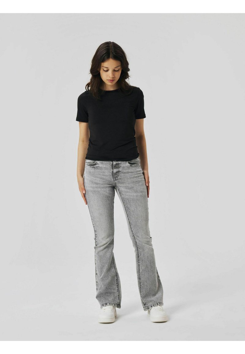 T-shirt nera a maniche corte abbinata a jeans a campana grigi chiari e sneakers bianche. L'outfit presenta un design aderente e tessuti morbidi.