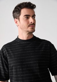 Sort t-shirt med korte ærmer, vandrette hvide striber, rund halsudskæring og blød tekstur. Designet til en afslappet pasform.