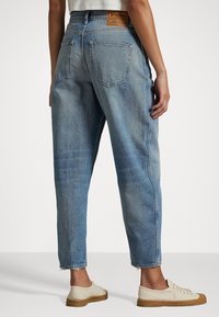 Ljusblå denimjeans med avslappnad passform, fransad söm, två bakfickor och en brun läderetikett i midjan. Ett par krämfärgade skor.