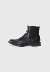 Black leather Chelsea boot with elastic side panels, rounded toe, and low stacked heel. Features red pull tab and subtle branding on the side.