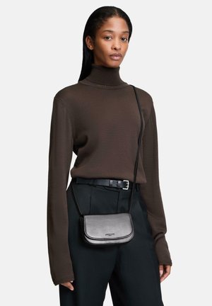 Schwarze lederne Umhängetasche mit einem schlanken, minimalistischen Design, das eine geschwungene Form und schlichte Hardware aufweist. Getragen über einem braunen Rollkragenpullover und einer Hose.