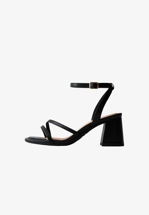 Zwarte sandaal met open teen, drie dunne bandjes, verstelbare enkelband met gouden gesp en een blokhak van gemiddelde hoogte.