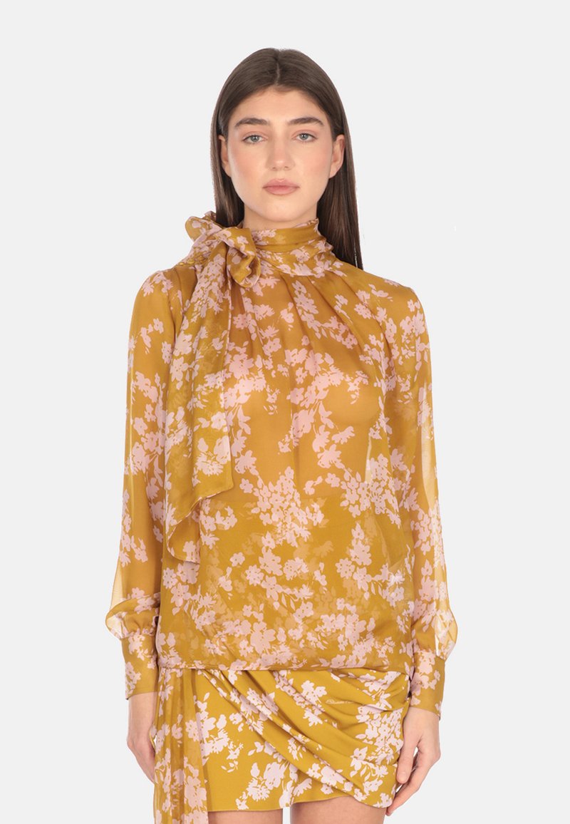 Blusa floreale gialla con maniche lunghe, tessuto morbido, colletto alto e dettaglio a fiocco al collo; presenta motivi floreali rosa su tutto.