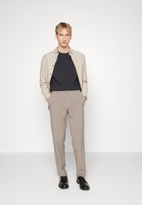 Cămașă bej deschis cu nasturi, tricou bleumarin, pantaloni gri deschis și pantofi negri. Textură fină, croială ajustată și elemente de design minime.