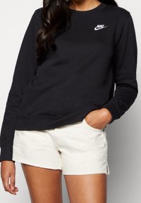 Czarna bluza z bawełny o mieszanym składzie, z okrągłym dekoltem i białym logo Nike. Zestawiona z szortami w kremowym kolorze z postrzępionymi brzegami.