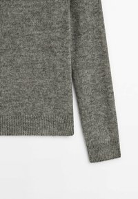 Manche et partie basse du torse d'un pull en tricot gris, montrant des poignets et un ourlet côtelés sur un fond blanc uni.