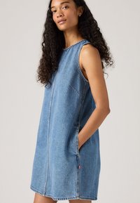Denim sleeveless dress in light blue with a straight cut, features side pockets and a raw hem. Contrast stitching and a logo tab detail.