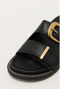 Black leather slide sandal with two wide straps and a gold-colored buckle. Features a textured footbed and a stitched black sole.