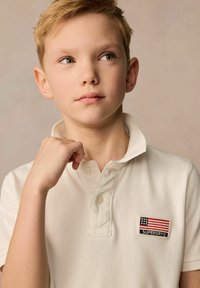Vit polo t-shirt med textilstruktur, utrustad med en knappad krage och en patch av den amerikanska flaggan med texten "SUPERDRY".