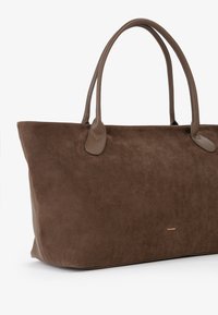Borsa tote in suede marrone con due manici coordinati. La parte anteriore presenta un logo discreto e una texture liscia, con una forma strutturata.
