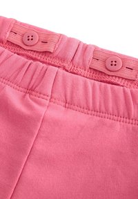 Bukser med pink bomuldslinning, der har en knaplukning og samlet elastikdetaljer. Teksturen er glat med ensartet syning.