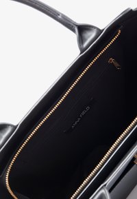 Svart väsk av konstläder med gulddragkedja, innerfack och textilfoder; har en etikett som säger "ANNA FIELD."