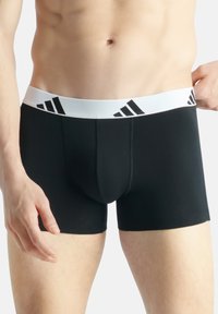 Boxer shorts pretos elásticos com uma cintura branca, apresentando detalhes do logotipo preto da Adidas. Tecido suave com um design ajustado.