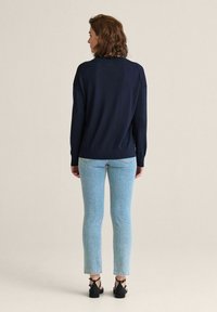 Marinblå stickad tröja med avslappnad passform, ihop med ljusblå formade jeans och svarta sandaler med ankelslingor.