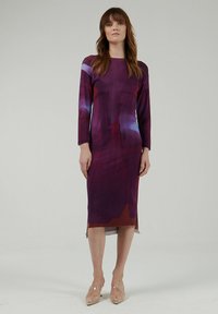 Vestido de manga larga en tela morada con patrones de colores abstractos. Corte ajustado, hasta la rodilla, con una abertura lateral para facilitar el movimiento.