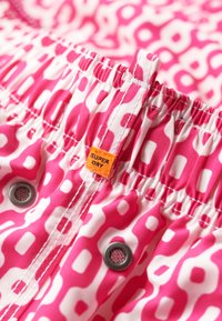 Short de bain à motif rose avec une taille élastique, doté d'un cordon de serrage, de boutons-pression argentés et d'une étiquette "Superdry" orange.