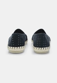 Fekete perforált anyagú slip-on cipők, szőtt juta talpakkal és fehér varrással, lekerekített orral és alacsony profilú kialakítással.