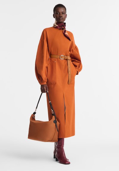 Rust-colored long dress with puff sleeves, cinched waist by a beige belt, and side slits. Accessories include a brown bag and maroon boots.