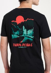 Černé bavlněné tričko s barevným designem horské krajiny, velkým červeným sluncem a textem "TWIN PEAKS populace 51 201" níže.