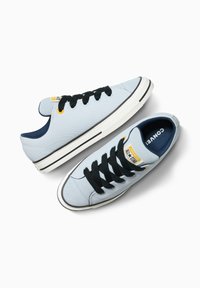 Sneakers in tela blu chiaro con lacci neri, suola in gomma bianca e fodera interna blu scuro a contrasto. Presentano una patch con logo sulla linguetta.
