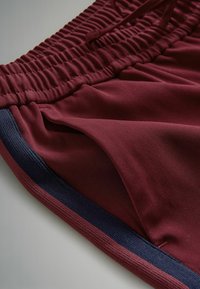 Bordové šortky s rebrovou textúrou, s námorníckym modrým lemom pozdĺž strán a elastickým pásom so šnúrkou.