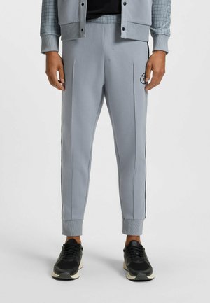 Helle graue Sportjogginghosen mit einem elastischen Bund, seitlichen Streifen und Bündchen an den Knöcheln, kombiniert mit schwarzen strukturierten Sneakern.