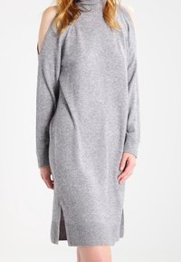 Robe grise en maille avec un col roulé et un design épaules dénudées. Comprend des manches longues et des fentes latérales, fabriquée en matériau doux et léger.