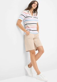 Gestreepte polo in pastelkleuren met kraag, gecombineerd met beige shorts. Witte sneakers maken de casual outfit compleet.