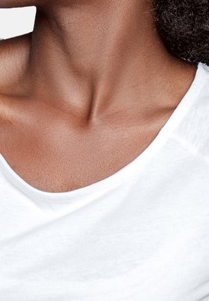 Gros plan sur le cou et le haut de la poitrine d'une personne portant une chemise blanche, avec des cheveux bouclés foncés partiellement visibles sur le côté.