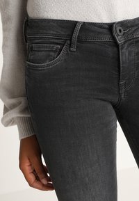Dunkelgraue Jeans aus Denim mit einem enganliegenden Design im Five-Pocket-Stil, sichtbaren Nähten und einem Knopfverschluss an der Taille.