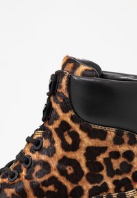 Ankle boty s leopardím vzorem vyrobené z měkkého kožíšku, s černými koženými akcenty, kulatými tkaničkami a šestiúhelníkovými oczky pro bezpečné zapínání.