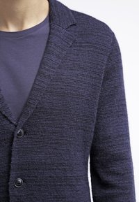 Mörkblå cardigan i strukturerad stickning, med en notch-krage, två knappar och lagd över en matchande blå t-shirt.